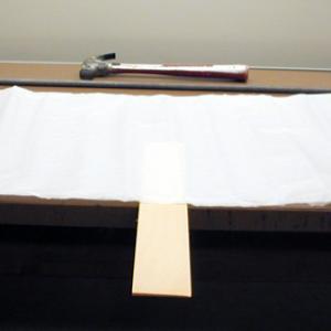 Place the board so that about 6 inches extends beyond the end of the table. Place the tissue paper over the portion of the board on the table making sure that the paper is smoothed and wrinkle free against the table. Strike sharply with a hammer at the end of the board. The board should break without disturbing the tissue paper.