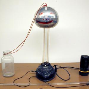 Set the apparatus as shown. Retract the metal spike and start the generator. Notice that there is charge buildup but no arcing between the spheres. Stick the spike out of the ball and point towards the generator and note the arcing. Turn the spike away from the generator and observe the corona. This is best observed in a darkened room. Refer to Eb - 2 for charge sign information. In our case the Van de Graaff generator should have a negative charge.  