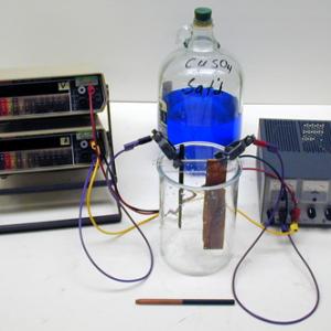 Pour the saturated copper sulfate solution into the battery jar so that it covers a good portion of the suspended electrodes. Insert the electrodes suspended from the Plexiglas rod and connect them to the power supply as shown. The resistor is inserted between the positive and negative outputs of the power supply to prevent shorting . Turn on the power supply and apply the desired voltage. The carbon electrode will become coated with copper in a short time.