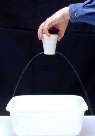 hand holding a Styrofoam cup with two Holes with water coming out over a catch basin