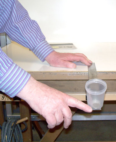 person holding a metal ruler on a table, transparent cup with coin